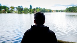Symbolbild: Ein Mann steht am Ufer eines Sees und schaut in die Ferne.