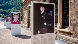 Open-Air-Ausstellung "We AHR strong" in Ahrweiler: Nacheinander aufgereihte Steelen mit Porträtfotos und Zitaten vor einem Gebäude.