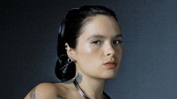 Portraitfoto der kanadischen Sängerin Saya Gray vor grauem Hintergrund.