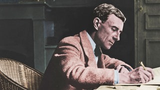 Maurice Ravel in Korbstuhl an Schreibtisch sitzend