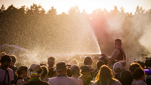 Ein Sicherheitsdienst-Mitarbeiter besprüht bei hochsommerlichen Temperaturen Festivalbesucher auf dem Gelände vom Hurricane Festival mit Wasser.