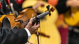 Bildausschnitt mit Fokus auf die Hand eines älteren Mannes, der eine Violine hält