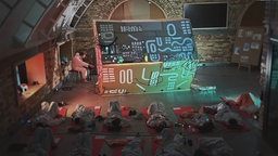 Kinder und Jugendliche liegen auf roten Matten vor der "Soundmachine" des Künstler-Kollektiv "Art Helps".