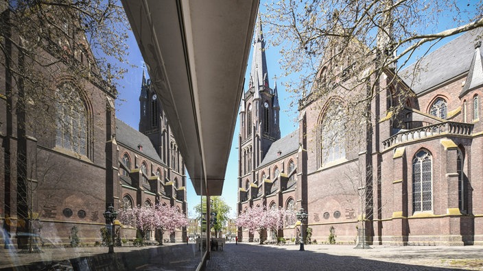 Außenansicht der Basilika Sankt Marien in Kevelaer, die sich in einer Glasfassade spiegelt.