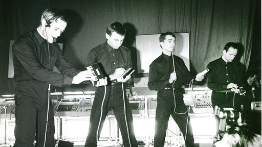 Schwarz-Weiß-Aufnahme der Mitglieder von Kraftwerk mit elektronischen Instrumenten.