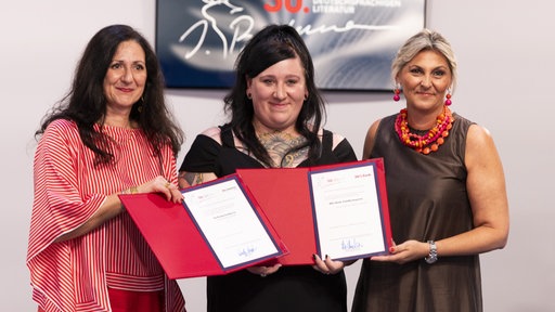 Bachmann-Preisträgerin Lena Schätte (M) präsentiert die Auszeichnung des Ingeborg-Bachmann-Preis' zusammen mit Intendantin Nadja Kayali (l.) und der Vorständin Renata Maurer-Nikolic (r.). 