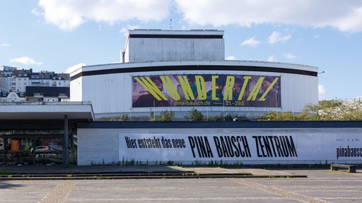 Außenansicht des Wuppertaler Schauspielhauses von 2024 mit einem Banner davor: "Hier entsteht das neue Pina Bausch Zentrum".