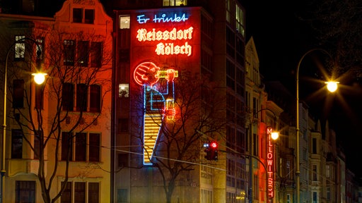 Das Reklame-Männchen mit dem Schriftzug "Er trinkt Reissdorf" leuchtet auf der Aachener Straße in Köln auf Höhe des Rudolfplatzes am 27.03.2017 - daneben leuchtet "Milliwitsch" am Theater.