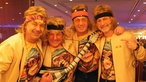 Vier Männer mit Stirnband, gelbem Sakko, Affen-T-Shirt und E-Gitarren-Attrappe freuen sich auf den Auftritt von Guildo Horn