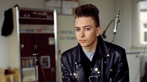 Alan Wilder 1984 in Berlin mit hochgestylten Haaren und Lederjacke vor Studiokulisse