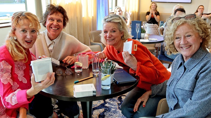 Vier Frauen an einem Tisch halten eine verpackte WDR 4-Bluetooth-Radiobox hoch