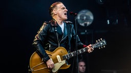 Bryan Adams singt und spielt Gitarre auf der Bühne