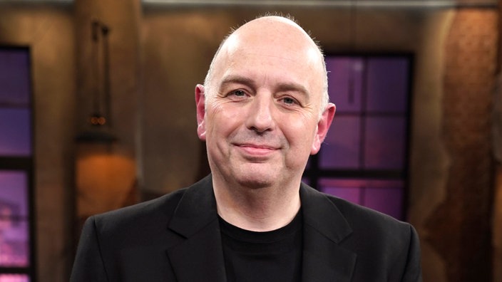 Frank Goosen lächelt freundlich in die Kamera. Er trägt ein schwarzes Oberteil mit schwarzem Sacko.