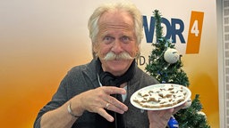 Henning Krautmacher beißt in einen Zimtstern. Im Hintergrund ist die Aufschrift "XMAS" zu sehen. 