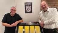 WDR 4-Hörer Markus aus Wegberg und Herbert, der ihm geholfen hat, Schallplatten auszustanzen, stehen neben Markus' alter Musikbox