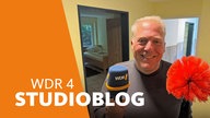 Lokalzeit-Reporter Dennis Burk mit Mikrofon und Putzinstrument in der Hand in einer Wohnung
