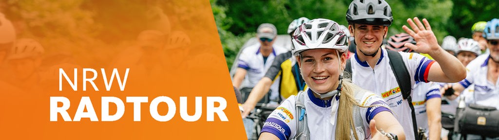 Blick von vorn auf eine große Gruppe von Radfahrern, vor einem Wald im Sommer fahrend, Radfahrer winken in die Kamera