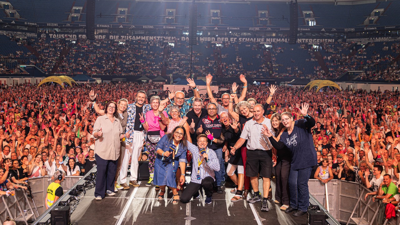 Die Gewinner einer Radio-Aktion stehen gemeinsam mit unseren Moderatoren auf der Bühne in der Arena auf Schalke