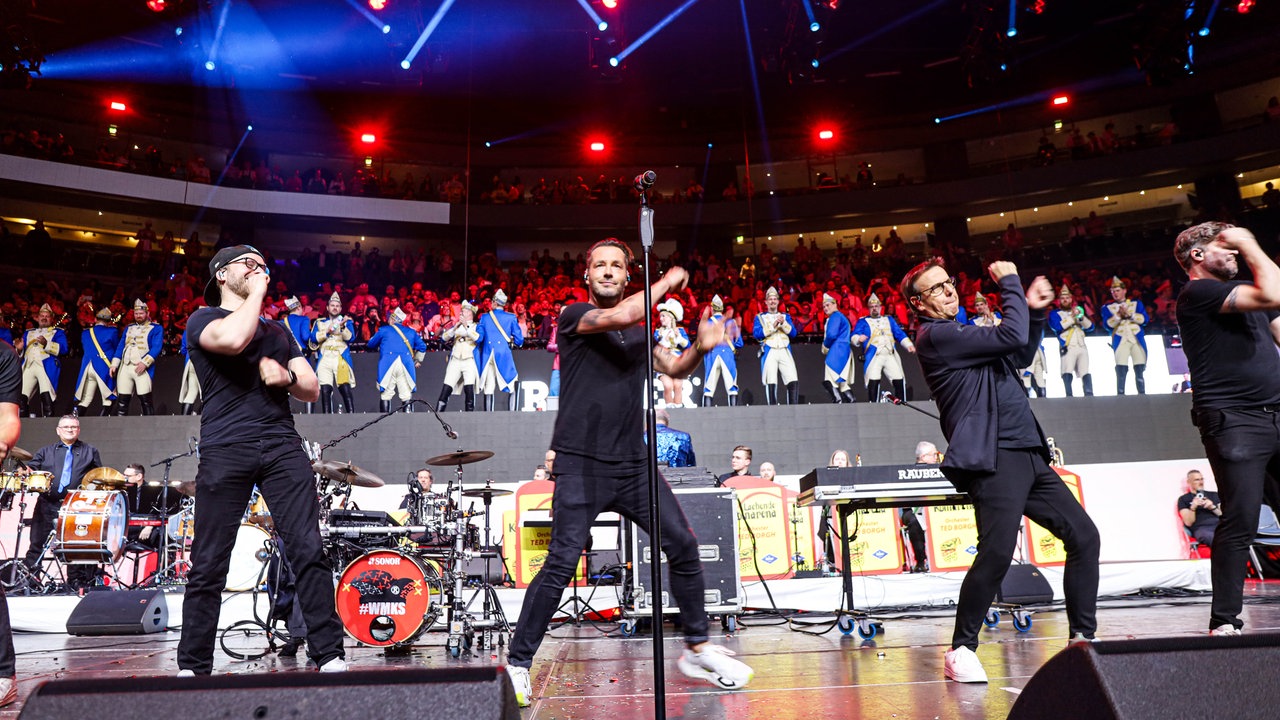 Lachende Köln Arena 2026: Die Mitglieder der Band Räuber stehen auf der Bühne in einer Reihe und tanzen zu ihrem Lied "Oben. Unten." 