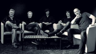 Schwarz-weiß Foto der Manfred Mann's Earth Band, auf Sesseln um einen Couchtisch herum sitzend.