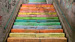 Eine bunte Treppe in Wuppertal. Auf den bunten Stufen stehen Wörter wie beispielsweise "aufblühen", "anziehend" und "Leidenschaft".