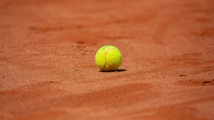 Ein gelber Tennisball liegt auf einem roten Ascheplatz