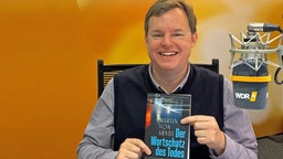 Mike Altwicker im WDR 4-Studio mit dem Buch "Der Wortschatz des Todes" von Martin von Arndt in den Händen