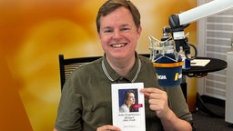Mike Altwicker im WDR 4-Studio mit dem Buch "Himmel ohne Ende" von Julia Engelmann in den Händen
