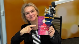 Elke Heidenreich sitzt im WDR 4 Studio mit dem Buch "Junge Frau mit Katze" von Daniela Dröscher in der einen Hand und einem Mikrofon vor sich