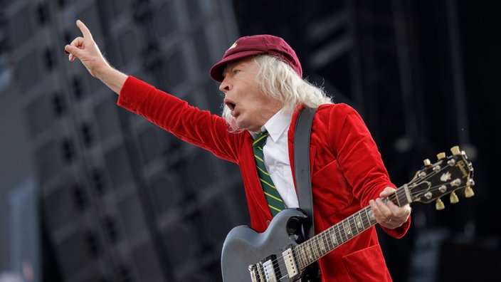 AC/DC-Leadgitarrist Angus Young 2024 bei einem Auftritt in Hannover. Er trägt seine berühmte rote Schuljungenuniform