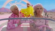 Filmszene aus dem Film "Barbie": Die Schauspieler Ryan Gosling und Margot Robbie sitzen in rosa Kleidung in einem rosa Auto.
