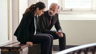 Professor Pohl (Christoph Maria Herbst, re.) sitzt neben Naima (Nilam Farooq, li.) auf einer Bank und spricht ihr Mut zu; in einer Szene aus dem Film "Contra".