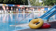Vor einer Rutsche in einem Freibad liegen zwei Schwimmringe, hinter dem Becken sieht man Sonnenschirme mit Stühlen