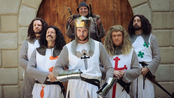 Sechs Schauspieler, verkleidet als König Artus, vier Ritter und ein Bauer, stehen vor der Kamera