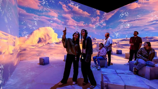 Menschen betrachten die Ausstellung, teilweise haben sie Kopfhörer auf den Ohren. Im Hintergrund sind große Bilder von Polarlandschaften.