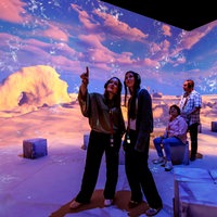 Menschen betrachten die Ausstellung, teilweise haben sie Kopfhörer auf den Ohren. Im Hintergrund sind große Bilder von Polarlandschaften.