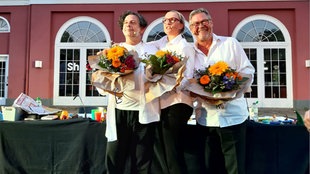 Drei Personen mit Blumensträußen auf der Bühne