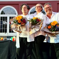 Drei Personen mit Blumensträußen auf der Bühne