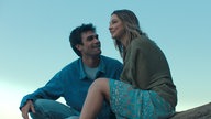 Eine Szene des Films "Liebe findet uns": Die Schauspieler KJ Apa und Madelyn Cline sitzen lächelnd nebeneinander vor einem blauen Himmel