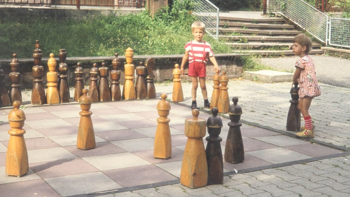 Zwei Kinder spielen mit den Figuren eines Riesenschachspiels (1977)