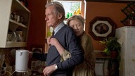 Eine Szene aus dem Film "Wer wir sind und wer wir waren": Grace (Annette Bening) und ihr Ehemann Edward (Bill Nighy) in der Küche. Er blickt ernst geradeaus in die Ferne, sie hat ihre Arme von hinten um ihn gelegt und schmiegt sich an seinen Rücken.