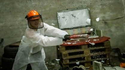 Eine Frau mit einem weißen Overall bekleidet und Helm auf dem Kopf zerstört mit einem Baseballschläger Dinge in einem Rage Rool