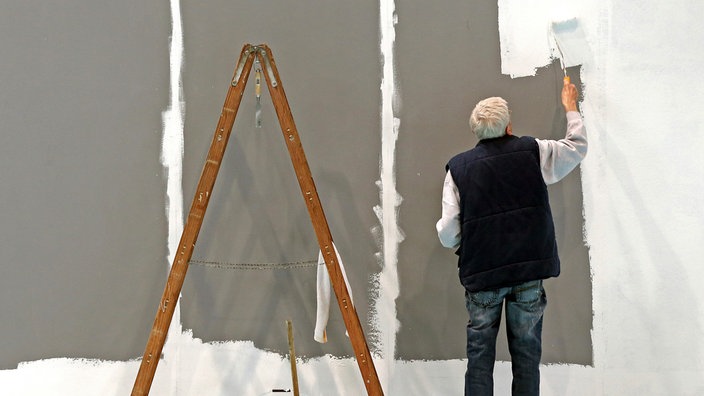 Ein älterer Mann streicht auf der Leipziger Messe eine Wand