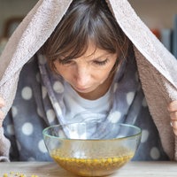 Eine Frau inhaliert über einer Glasschüssel mit Kamillenblüten.