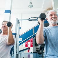 Eine Frau und ein Mann über 50 sitzen auf Fitnessgeräten und stämmen Gewichte