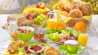 Gedeckter Frühstückstisch mit Brötchen, Croissants, Früchten, Eiern und Saft