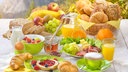 Gedeckter Frühstückstisch mit Brötchen, Croissants, Früchten, Eiern und Saft