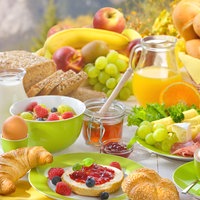 Gedeckter Frühstückstisch mit Brötchen, Croissants, Früchten, Eiern und Saft