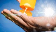 Es wird Sonnencreme auf eine Hand gemacht. Im Hintergrund scheint die Sonne