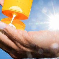 Es wird Sonnencreme auf eine Hand gemacht. Im Hintergrund scheint die Sonne